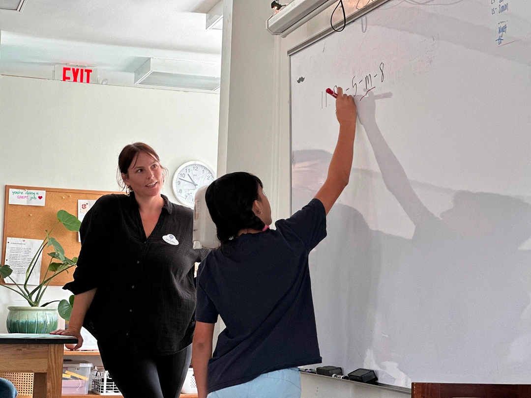 Teacher watching a student solve a math problem on a classroom whiteboard