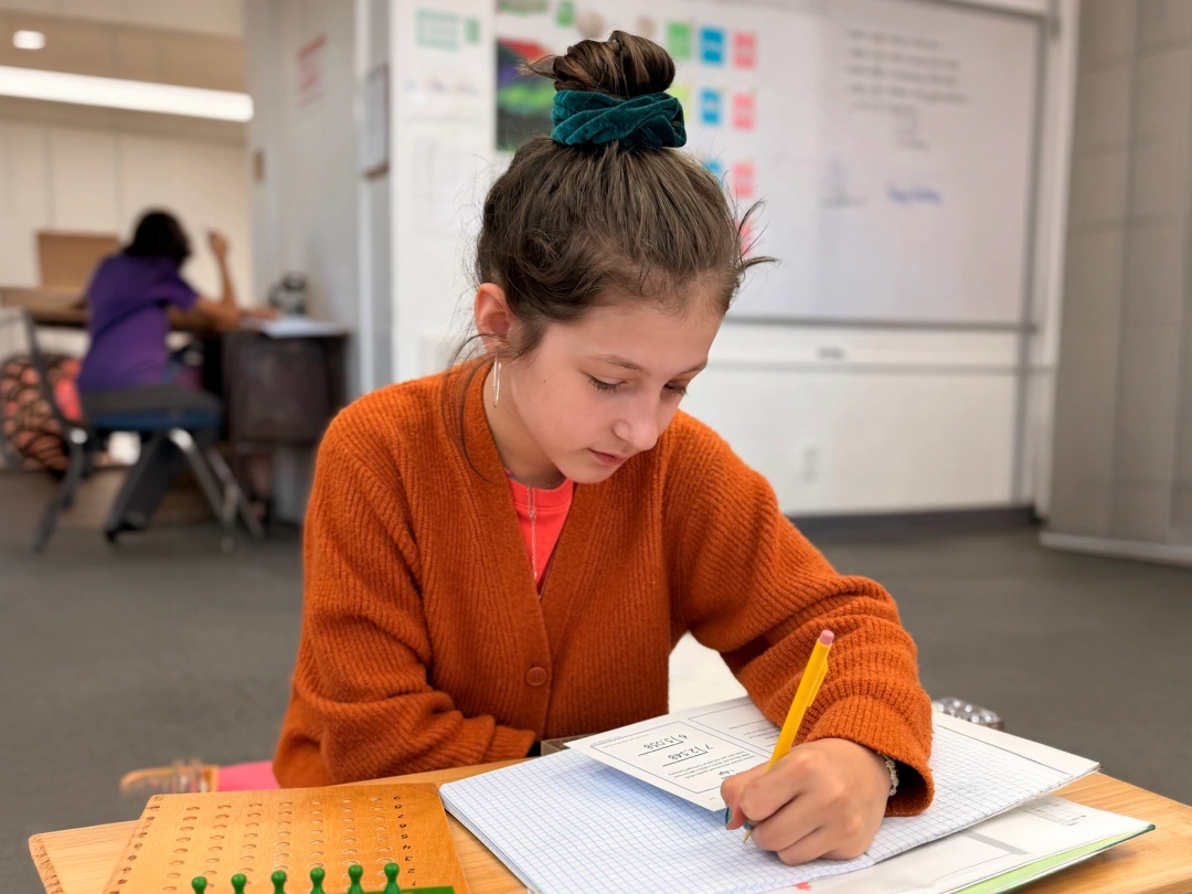 Child writing in a notebook at a classroom desk